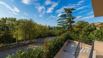 Un balcon donnant sur une rue bordée d’arbres et sur un ciel bleu dégagé.