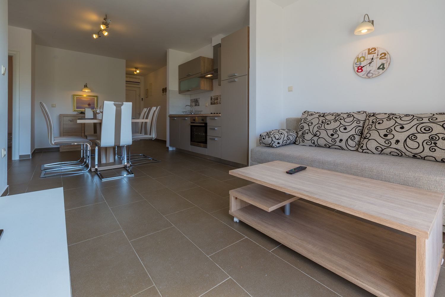 A modern living room with a sofa, a coffee table, and a dining area with chairs and a table.