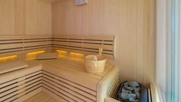 A sauna with wooden benches, a wooden bucket, and a stone-filled container.