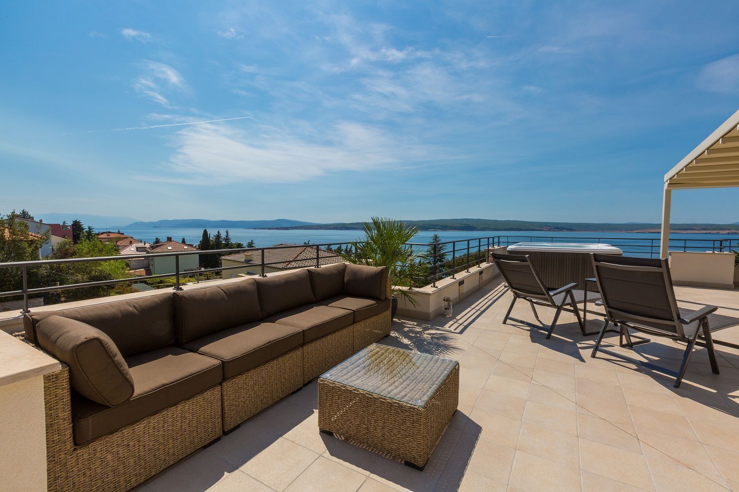 A terrace with a sofa, chairs, and a table overlooking a scenic view of the sea and mountains.