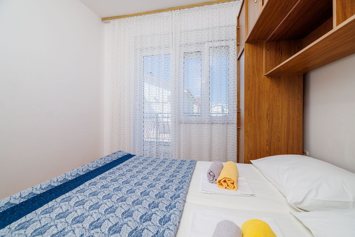Een slaapkamer met een bed, een raam met kantgordijnen en een houten hoofdeinde.