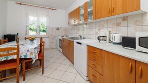 Una cucina con mobili in legno, un piano di lavoro bianco, lavastoviglie, piano cottura e una zona pranzo con tavolo e sedie.