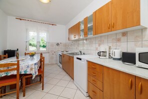 A kitchen with wooden cabinets, a white countertop, a dishwasher, a stove, and a dining area with a table and chairs. - Large apartment just 400 metres from the beach with sea view, barbecue area, WiFi, air conditioning (Crikvenica)