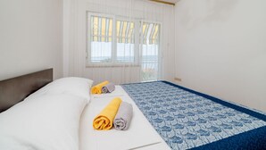 Camera d'albergo con un letto, due asciugamani arrotolati, una coperta a motivi e una finestra con tende.