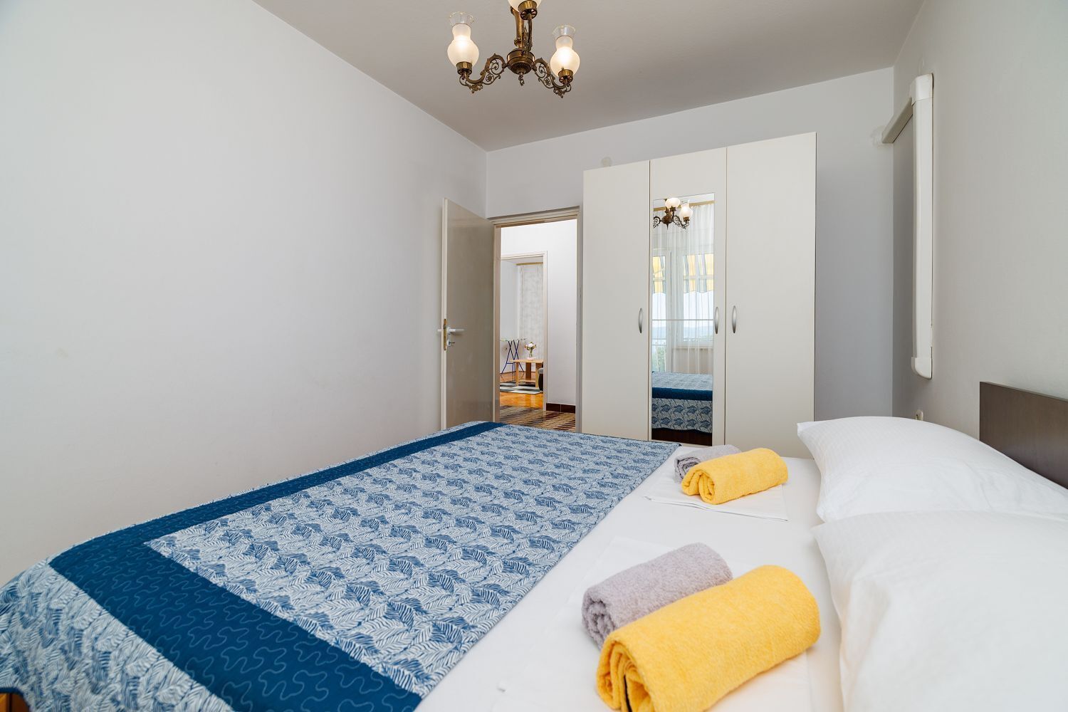 Quarto com cama, duas toalhas, um candelabro e uma porta que dá para outro cômodo.