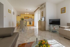 A modern living room with a sofa, TV, and a dining area with chairs and a table. - Dog-friendly apartment just 470 metres from the beach with cot and sea view (Povile)