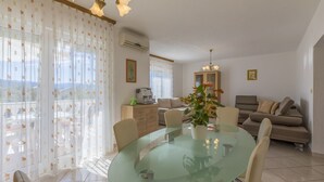 Een moderne woonkamer met een glazen eettafel, beige banken en een groot raam met gordijnen.