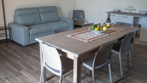 Un salon moderne avec un canapé gris, une table à manger avec des chaises et un coin cuisine doté de placards et d’un plan de travail.