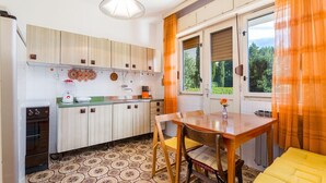 A kitchen with wooden cabinets, a dining table with chairs, and a view of greenery outside. - Rustic apartment just 100 metres from the beach with sea view, balcony, terrace, air conditioning (Crikvenica)
