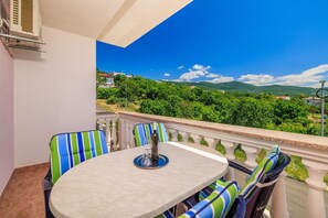 Ein Balkon mit Tisch und Stühlen, mit Blick auf eine üppige grüne Landschaft mit Hügeln und blauem Himmel.
