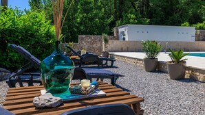 Ein Poolbereich mit Liegestühlen, einem Tisch mit einer Vase und Steinen sowie Topfpflanzen.