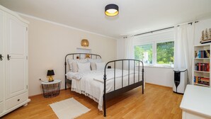 Ein Schlafzimmer mit Bett, Nachttisch, Lampe und einem Fenster mit Vorhängen.