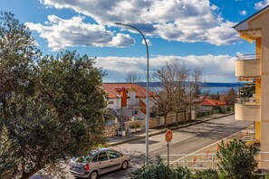 A street view with a car parked at a stop sign, a clear blue sky, and buildings with red-tiled roofs. - Dog-friendly studio apartment just 250 metres from the beach with sea views (Novi Vinodolski)