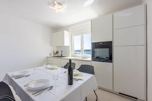 Una cucina moderna con mobili bianchi, un tavolo da pranzo per due persone e vista mare attraverso ampie finestre.