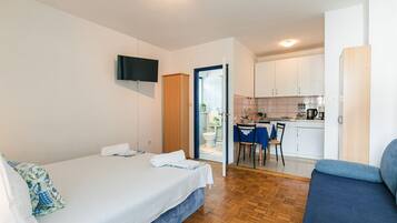 A hotel room with a bed, a TV mounted on the wall, a kitchenette, and a dining area.