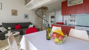 A modern living room with a sofa, a dining table with a fruit bowl, and a kitchen area with red cabinets and a stove. - Bright apartment just 400 metres from the beach with stunning sea views and two bikes (Selce)