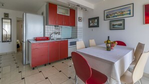 A modern kitchen with red cabinets, a dining table with chairs, and a chandelier. - Bright apartment just 400 metres from the beach with stunning sea views and two bikes (Selce)