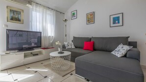 A modern living room with a grey sofa, a flat-screen TV, and a coffee table. - Bright apartment just 400 metres from the beach with stunning sea views and two bikes (Selce)
