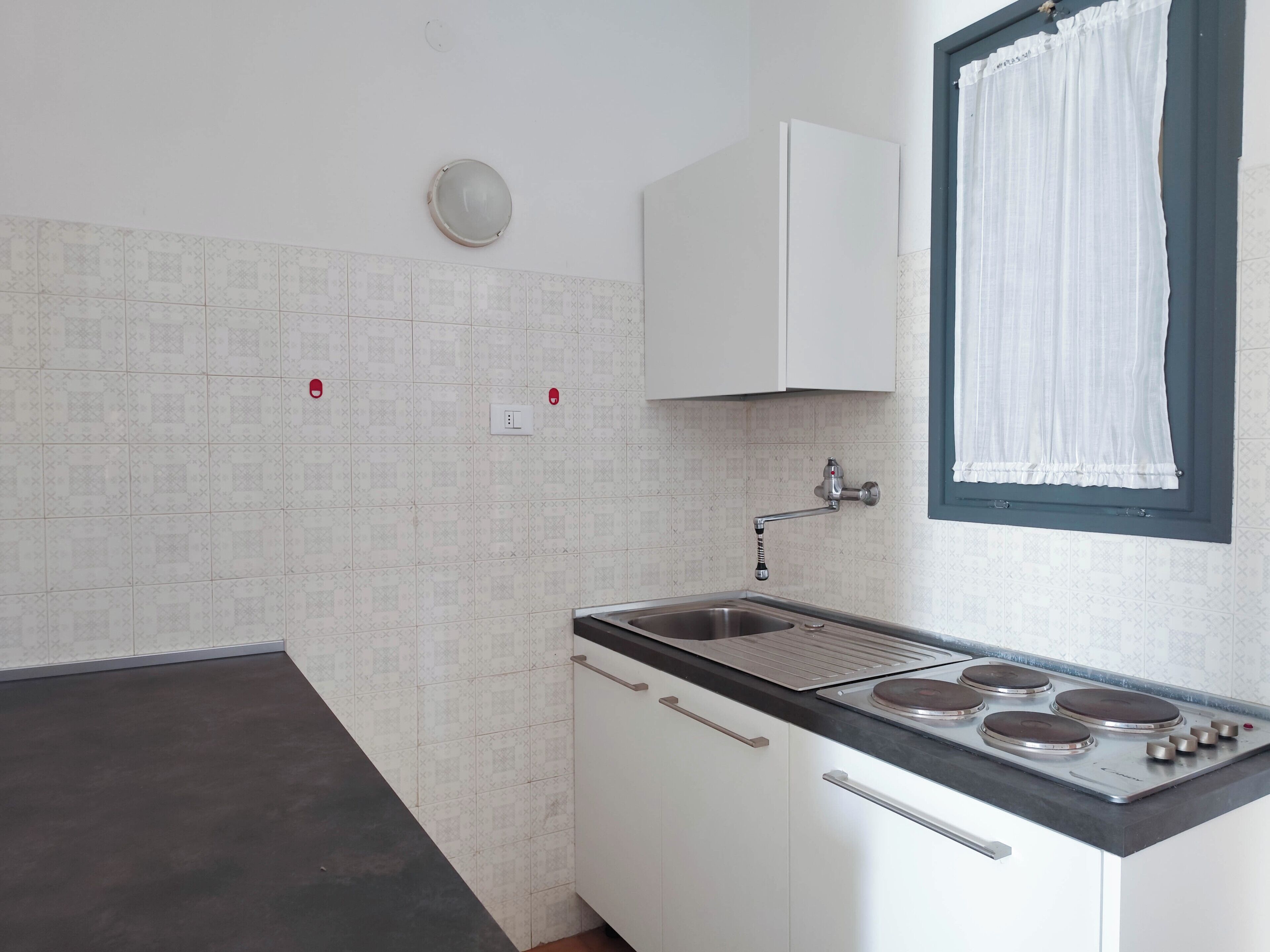Una piccola cucina con mobili bianchi, un lavandino in acciaio inossidabile e un fornello a gas.
