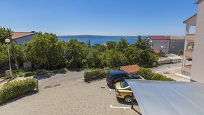 Ein Parkplatz mit zwei Autos, Blick auf das Meer und Gebäuden mit roten Dächern.