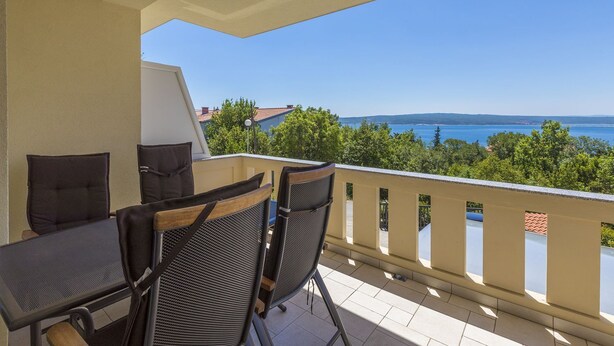 Ein Balkon mit zwei Stühlen und einem Tisch, der einen schönen Blick auf das Meer und die grüne Landschaft bietet.