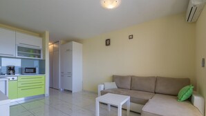 Ein modernes Wohnzimmer mit einem beigefarbenen Sofa, einem weißen Couchtisch und einer Küchenzeile mit Mikrowelle und Kaffeemaschine.