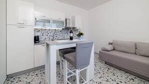 Een kleine keuken met witte kastjes, een aanrecht en een stoel.