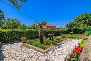 Ein Garten mit einer Statue, einer Palme und einem Haus im Hintergrund.