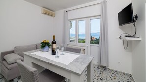 Een moderne kamer met een eettafel, een bank, een aan de muur bevestigde televisie en een raam met uitzicht op zee.