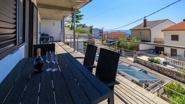 Een balkon met een tafel, stoelen en een fles wijn.
