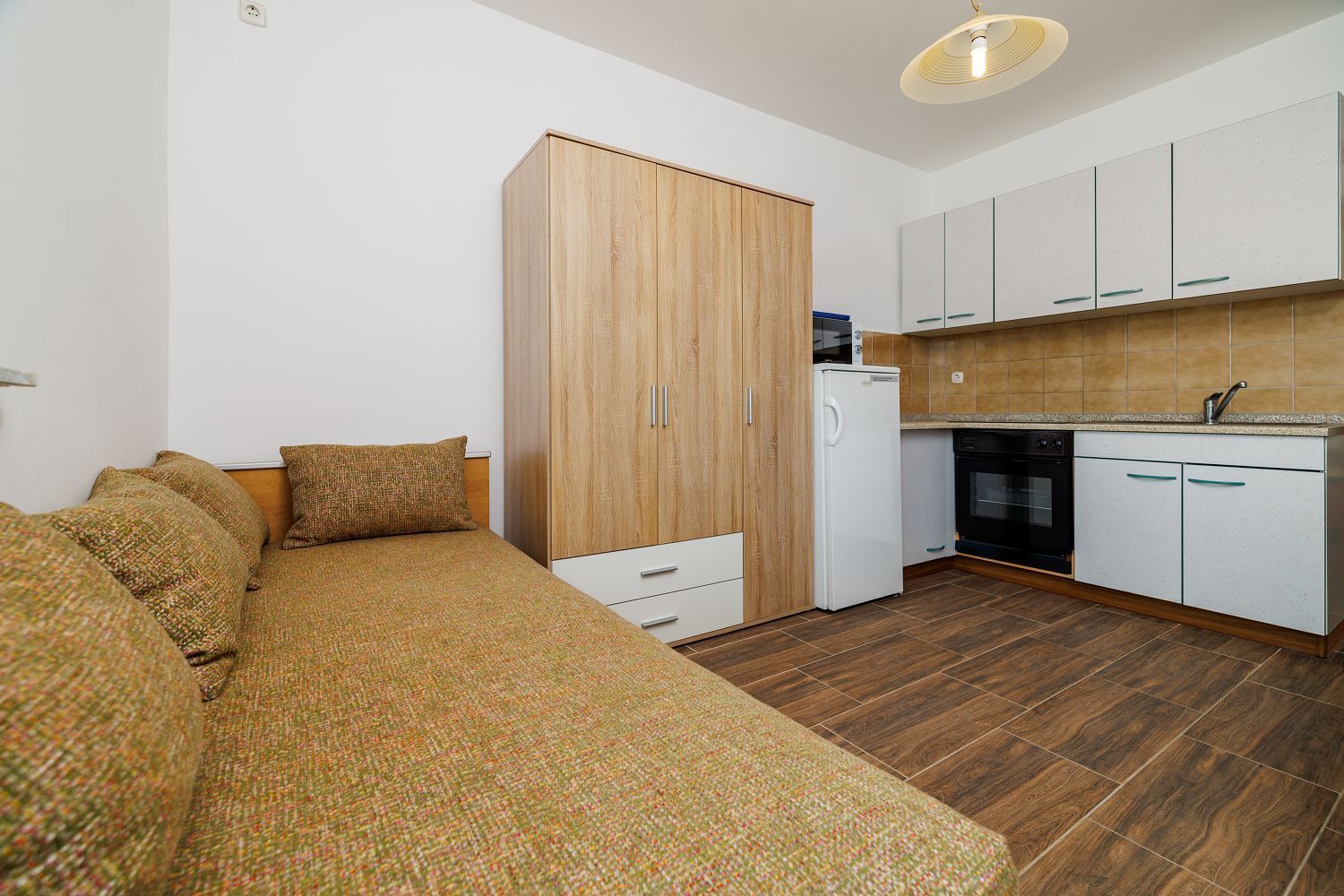 A compact bedroom with a bed, a wardrobe, and a kitchenette.