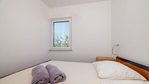 Een slaapkamer met een bed, een raam en een nachtkastje met een lamp.