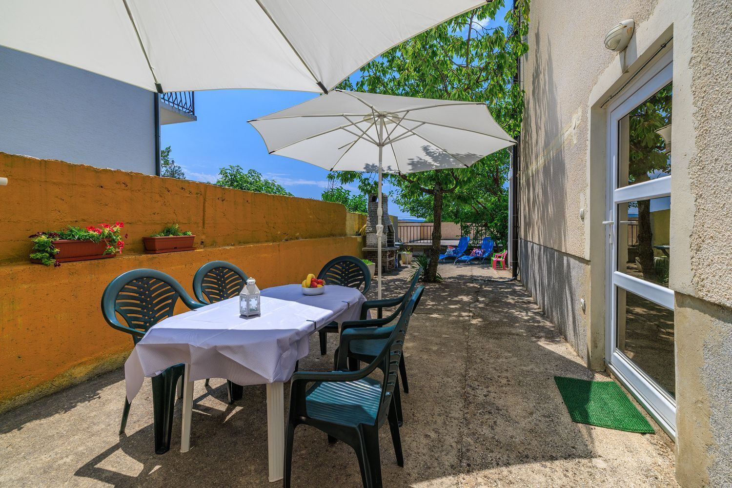 An outdoor patio with a table and chairs, a white umbrella, and potted plants on the wall.