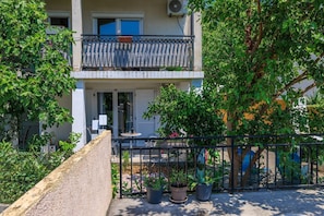 A two-story building with a balcony, potted plants, and a gravel pathway. - Comfortable apartment just 300 metres from the beach with deckchair, barbecue and parking space (Dramalj)