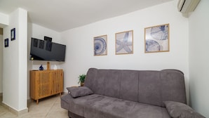Ein Wohnzimmer mit grauem Sofa, einem Holzschrank, einem Flachbildfernseher und drei gerahmten Kunstwerken an der Wand.