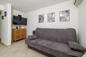 A living room with a grey sofa, a wooden cabinet, a flat-screen TV, and three framed artworks on the wall. - Comfortable apartment just 300 metres from the beach with deckchair, barbecue and parking space (Dramalj)