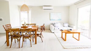 Una sala de estar luminosa con comedor, paredes blancas y un ventanal grande.