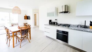Una cocina moderna con armarios blancos, encimera de granito y horno empotrado. Hay una zona de comedor con mesa y sillas de madera.
