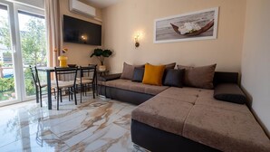 En moderne stue med en hjørnesofa, et spisebord med stole, et fladskærms-TV monteret på væggen og et stort vindue med gardiner.