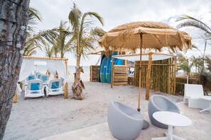 Ein Strandloungebereich mit Reetdachschirmen, Liegestühlen und Surfbrettern.
