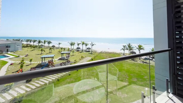 A balcony with a view of a beach, palm trees, and a playground. - Oceanfront Serenity -V5-3E- 2 bed, 2 bath (Punta Chame)