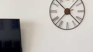 Ein modernes Wohnzimmer mit Flachbildfernseher, einer großen Wanduhr und einer dekorativen Fischskulptur auf einem kleinen Tisch.