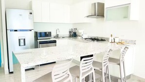 Eine moderne Küche mit weißen Schränken, einem Edelstahlkühlschrank, einer Mikrowelle, einem Geschirrspüler, einem Gasherd und drei weißen Barhocker.