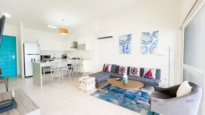 Ein modernes Wohnzimmer mit Sofa, Couchtisch und Essbereich mit Stühlen sowie einer Küche im Hintergrund.