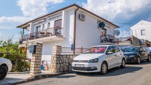 Ein zweistöckiges Gebäude mit Balkon, steinernen Eingang und einem weißen Auto davor.