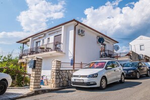 A two-story building with a balcony, a stone entrance, and a parked white car in front. - Quiet apartment close to the centre with private parking and washing machine (Novi Vinodolski)
