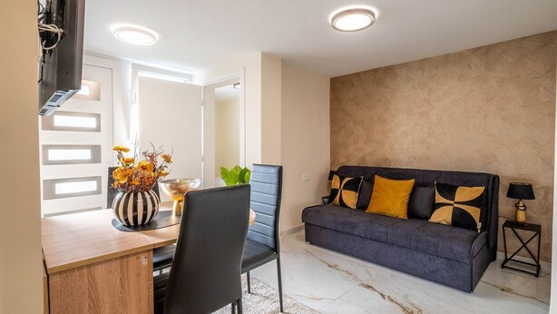 Ein modernes Wohnzimmer mit einer Couch, einem Esstisch mit Stühlen und einem an der Wand befestigten Fernseher.