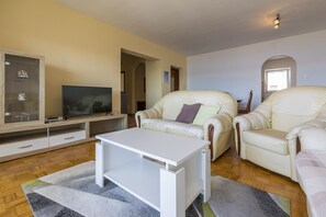 Ein Wohnzimmer mit Fernseher, zwei Ledersofas, einem weißen Couchtisch und einer Vitrine mit einem Schiffmodell.