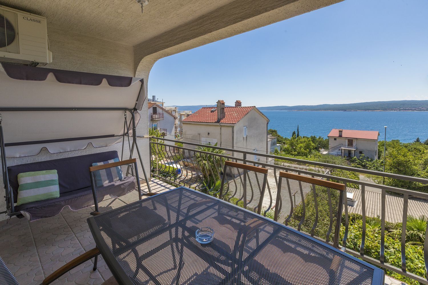 A balcony with a table and chairs, overlooking a coastal view with houses and a body of water.