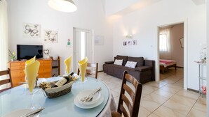 Un vaste espace de vie comprenant une table à manger pour deux personnes, un canapé et un téléviseur.